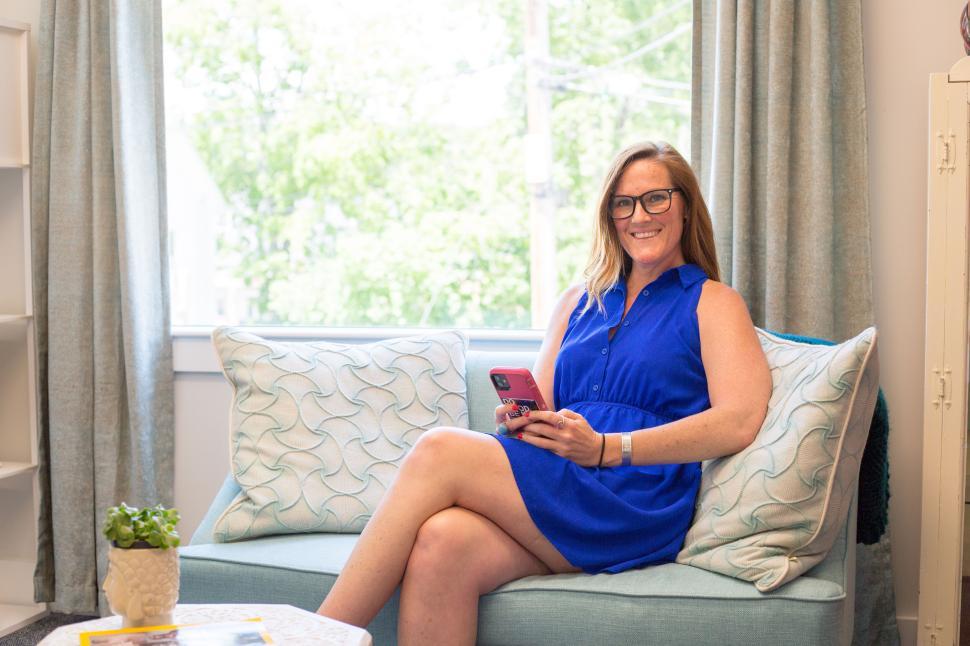 Free Image of Woman in blue dress holding phone and sitting on sofa 
