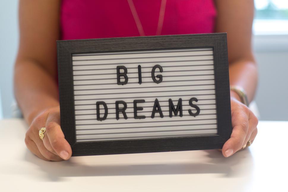 Free Image of Person holding a sign with the words  Big Dreams  on white table. 