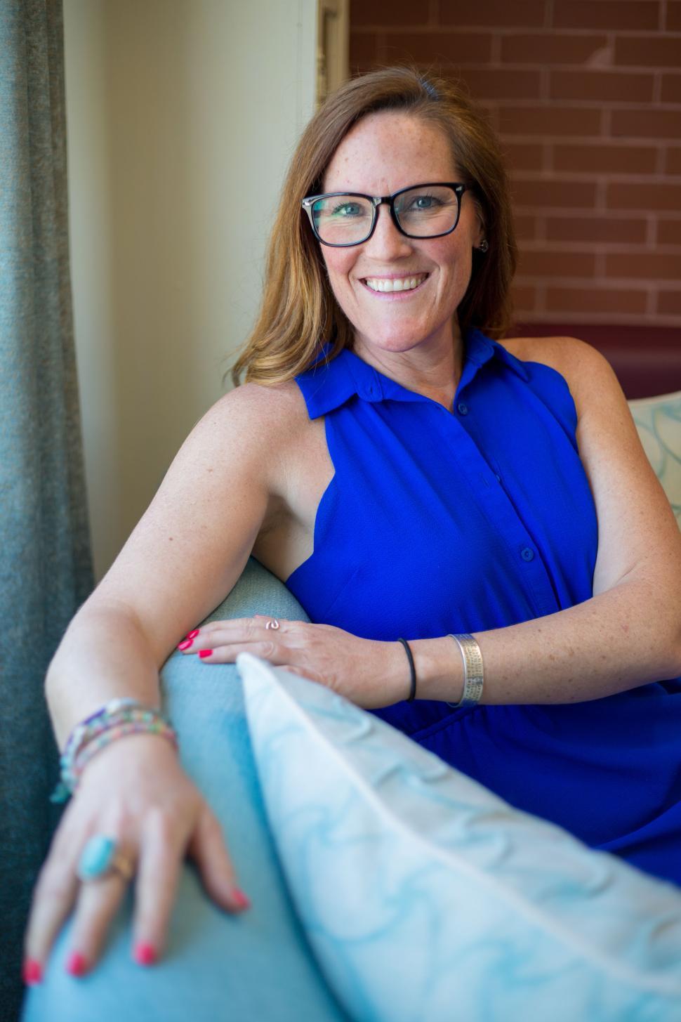 Free Image of Smiling woman in blue dress sitting in bright room 
