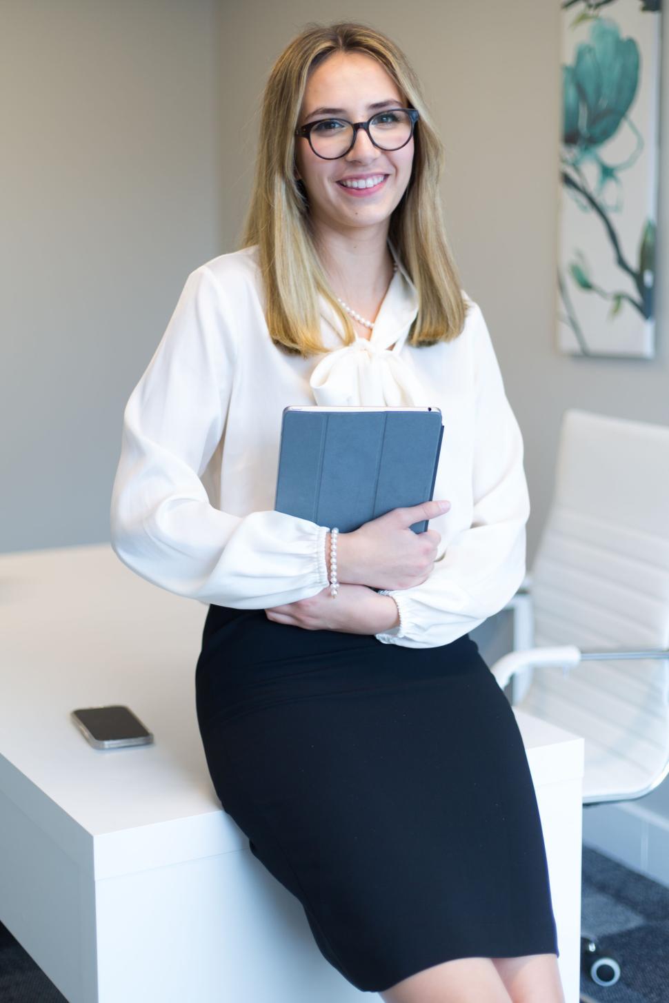 Free Image of Woman in office attire holding a tablet and smiling confidently. 