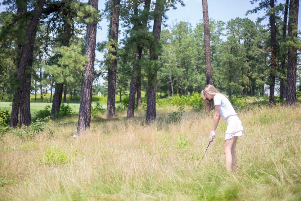 Free Image of Woman playing golf in an outdoor grassy field with trees 