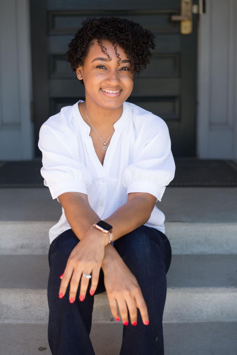 Free Image of Smiling woman sitting on steps outside a building on a sunny day. 
