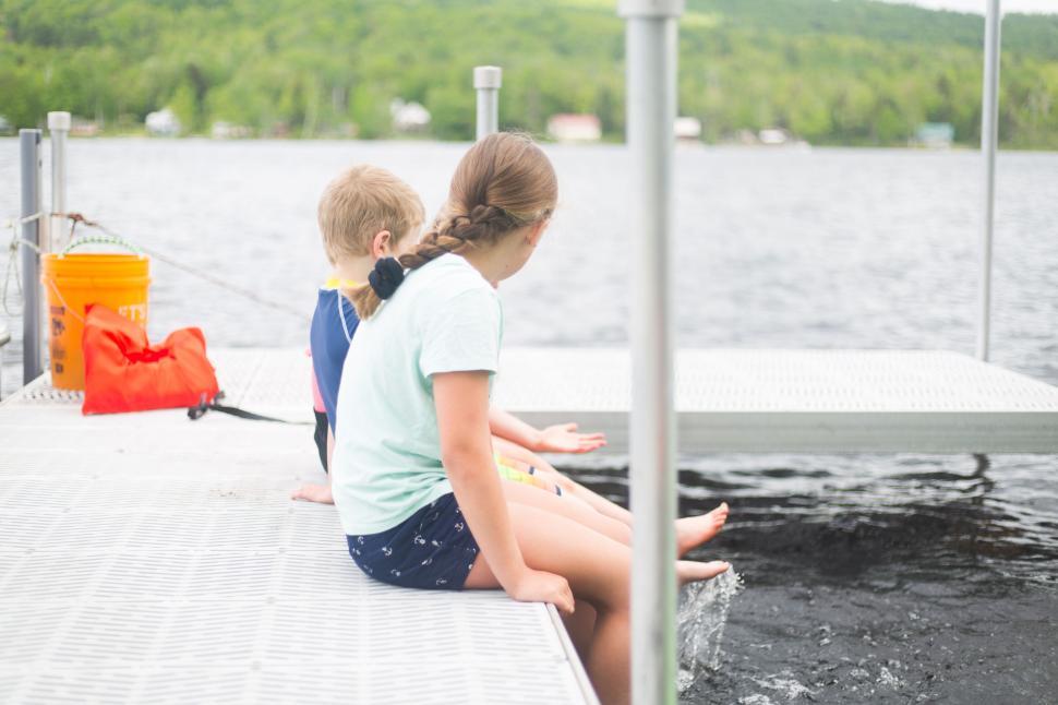 Free Image of Two children sitting on a dock by a lake engaged in conversation. 