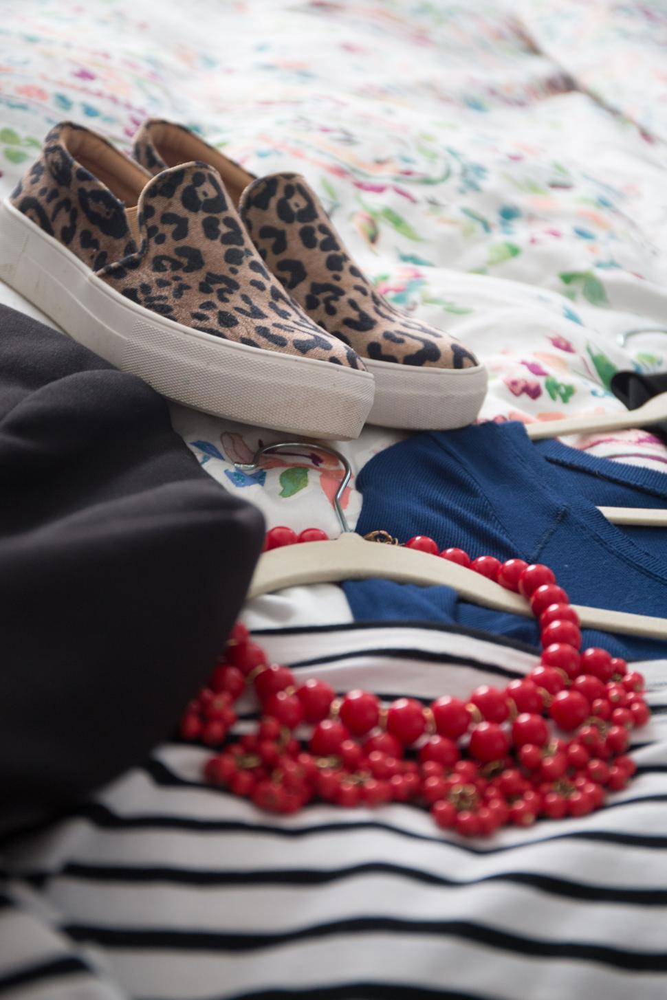 Free Image of A leopard print shoe, red necklace, and folded clothes on a bed. 