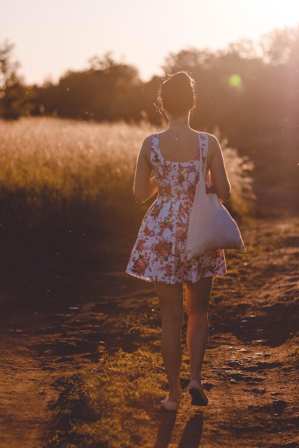 Free Image of Woman in floral dress walking in field path during sunset time. 