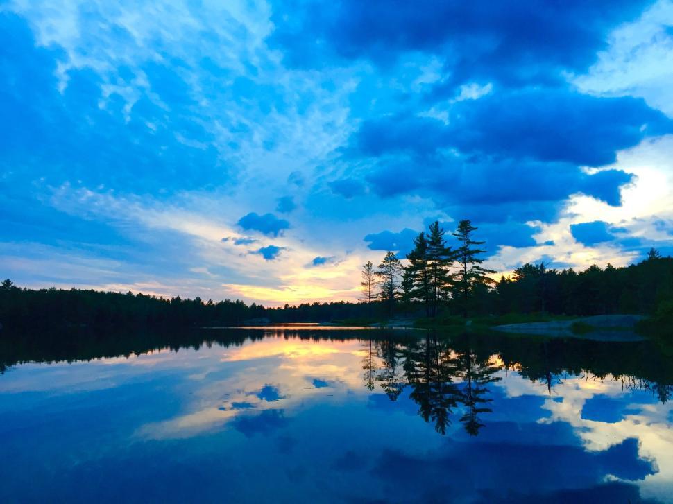 Free Image of Serene lake reflecting vibrant blue sky amidst dense tree line 