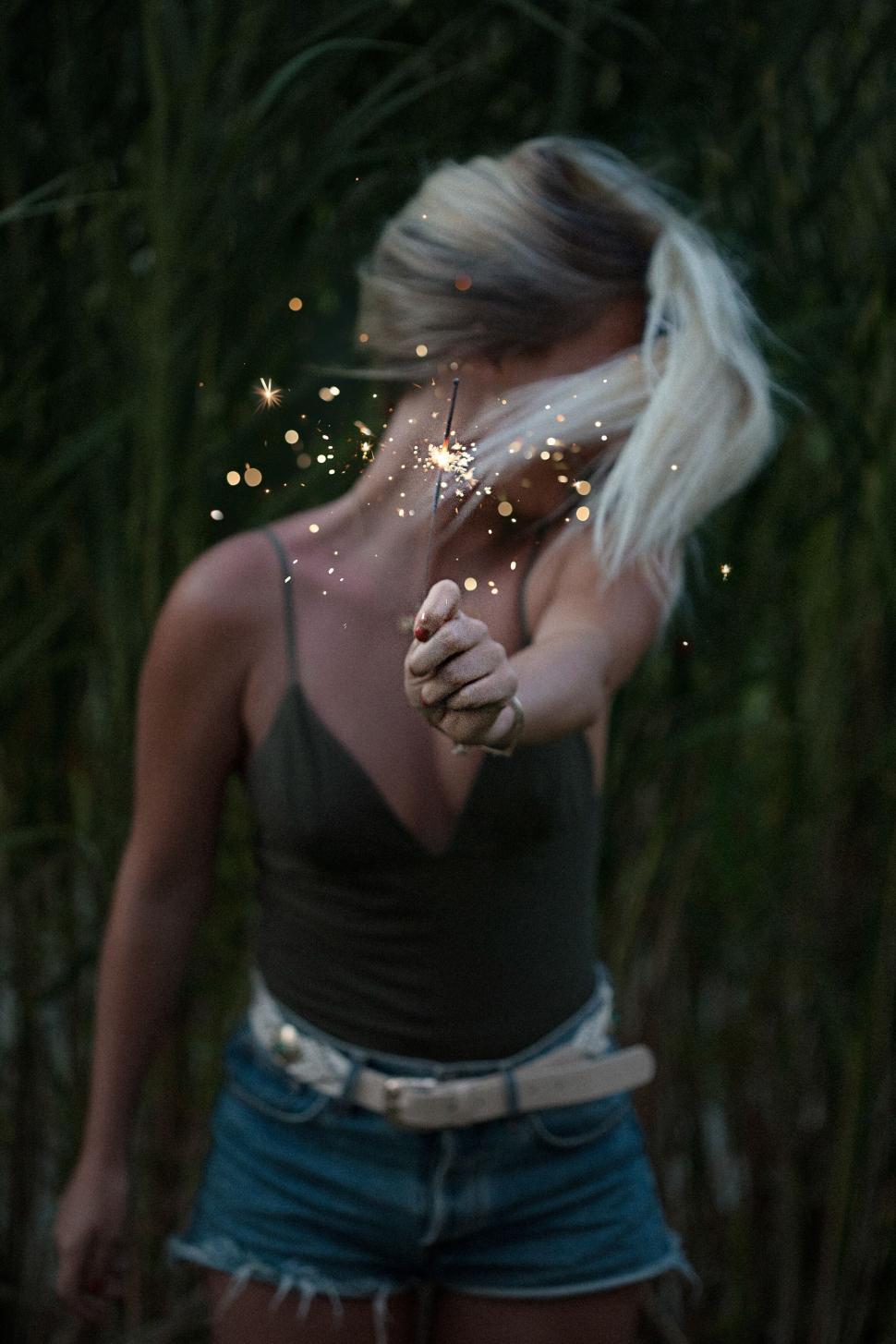 Free Image of Woman enjoying sparklers at night with a serene background 