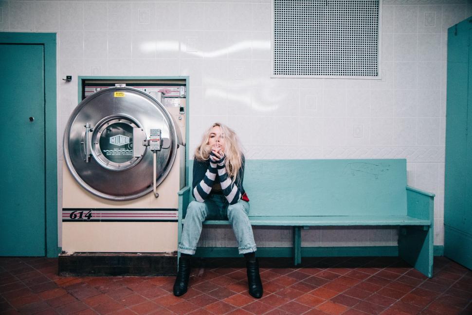 Free Image of Young woman in laundromat, sitting on a bench near washer 