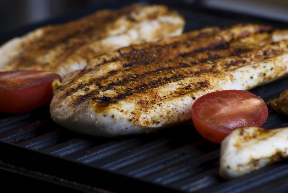 Free Image of Grilled chicken fillets with sliced tomatoes on a dark grill surface. 