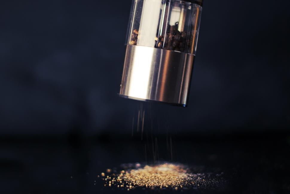Free Image of Pepper grinder dispensing freshly ground pepper onto a dark surface. 