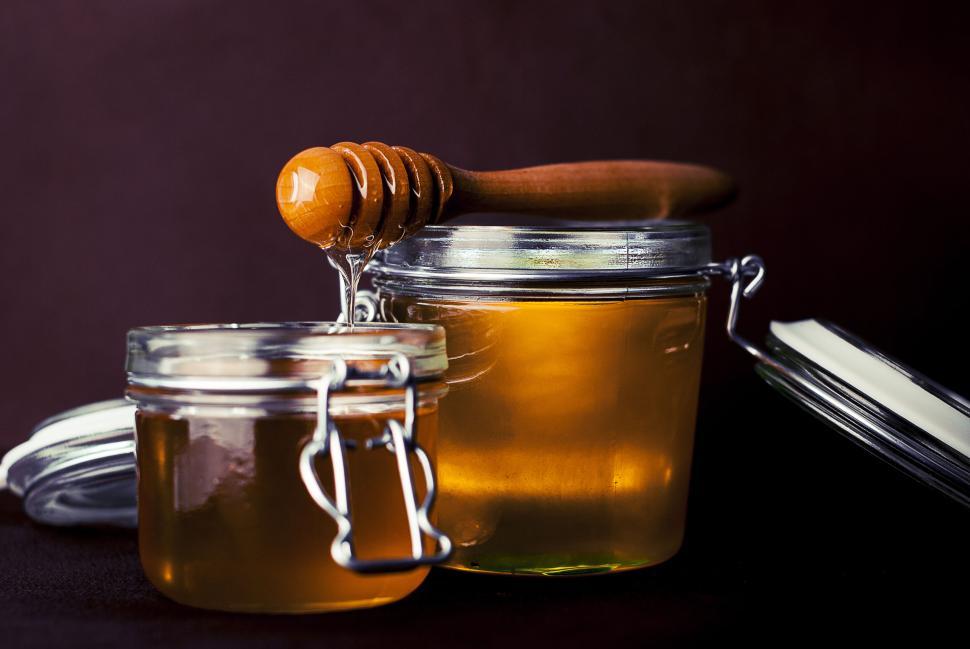 Free Image of Two glass jars filled with golden honey and a wooden honey dipper. 