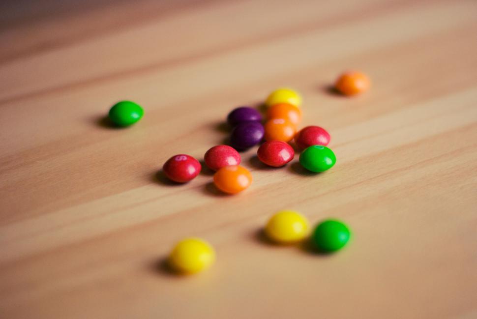 Free Image of Colorful candy pieces spilled on a wooden surface in close-up view. 