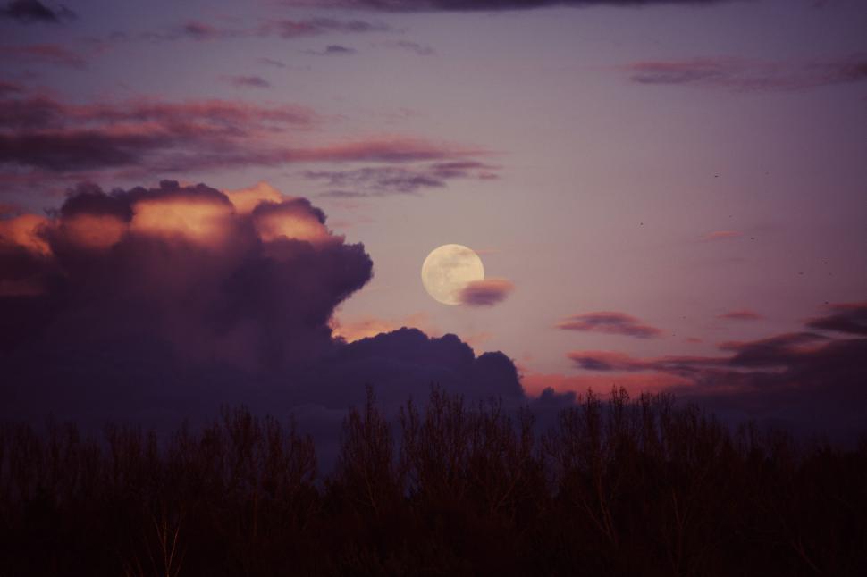 Free Image of Full moon rising behind dark clouds with a backdrop of vivid twilight. 