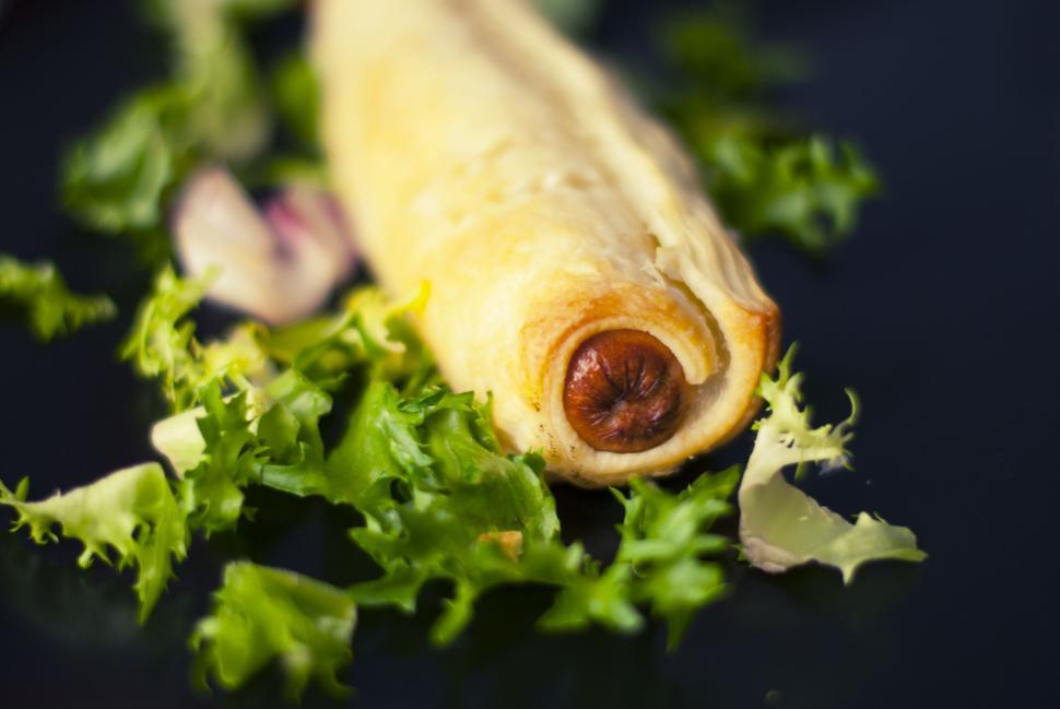 Free Image of Savory sausage roll placed on a bed of fresh greens, close-up image. 