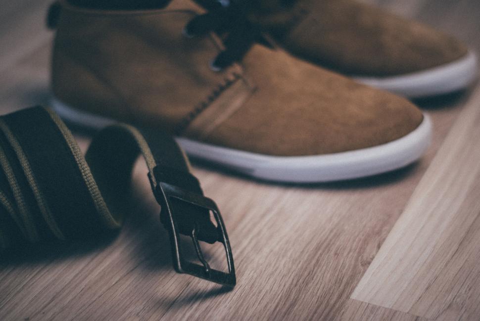 Free Image of Brown suede casual shoes and green belt on wooden floor in focus 