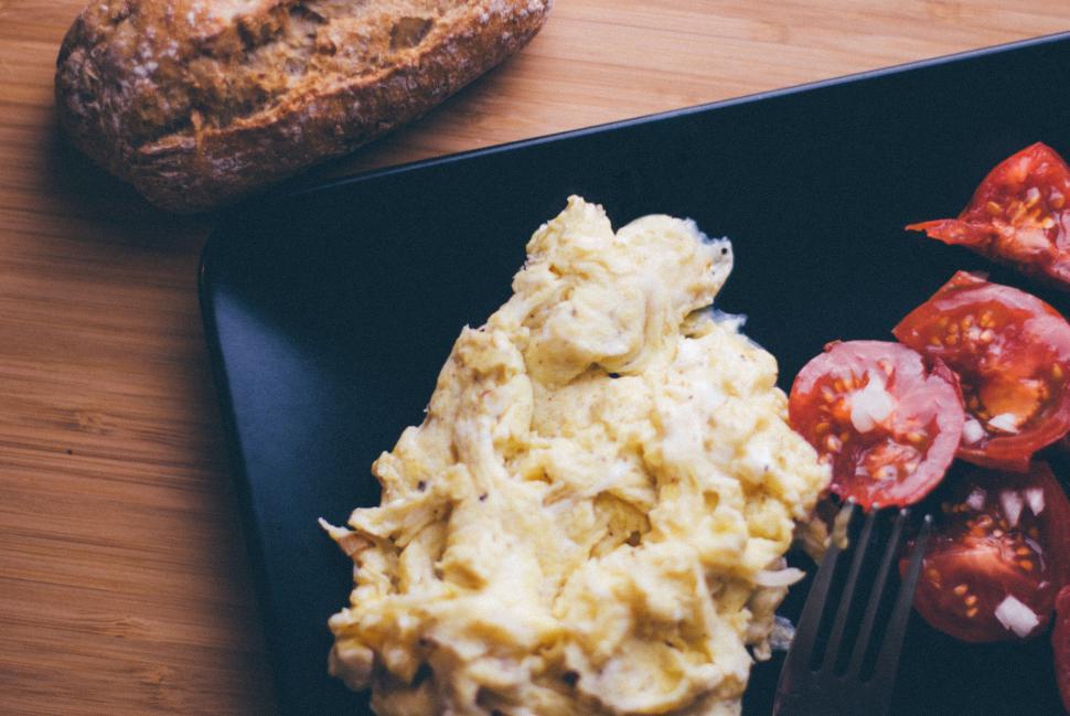Free Image of Scrambled eggs with tomatoes and bread on black plate, close-up. 