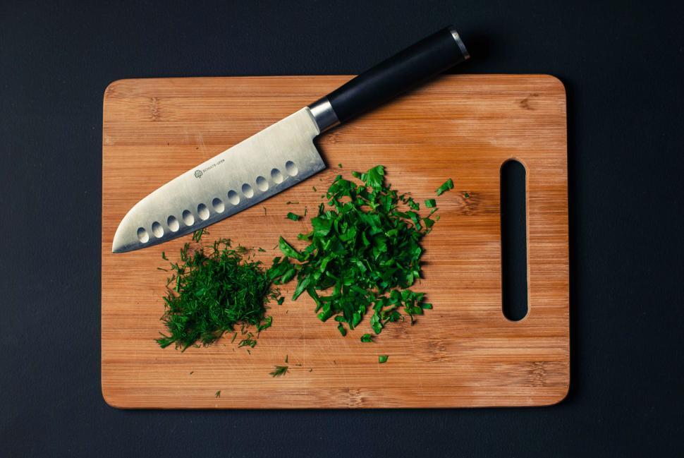 Free Image of Chopped green herbs on a wooden cutting board with a sharp knife 