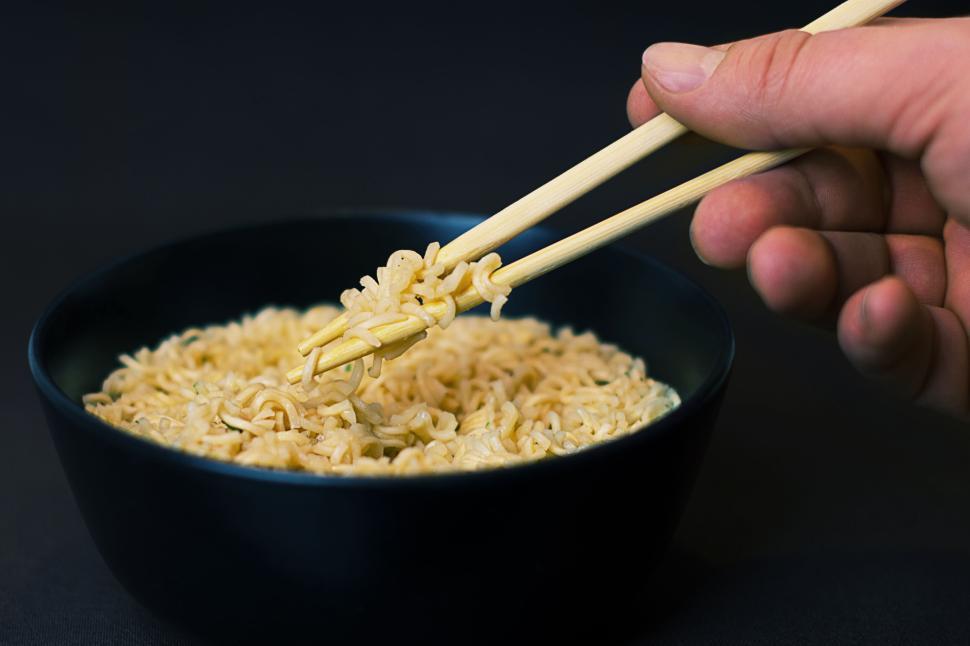 Free Image of Hand using chopsticks to eat noodles from a bowl on dark background. 