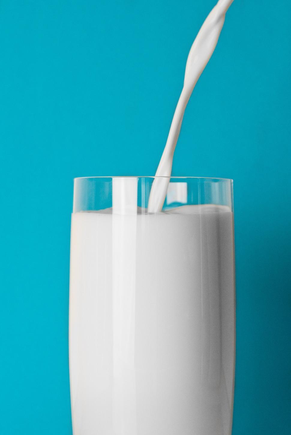 Free Image of Pouring milk into a tall glass against a vibrant turquoise background. 