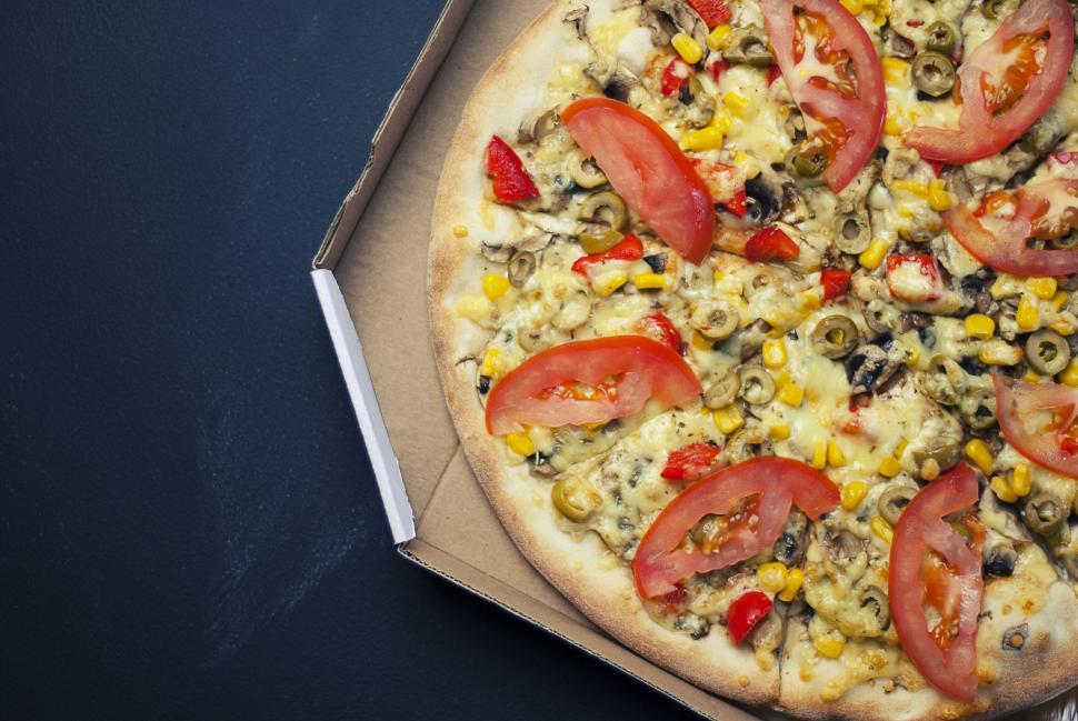 Free Image of Vegetarian pizza in a cardboard box with colorful toppings displayed. 