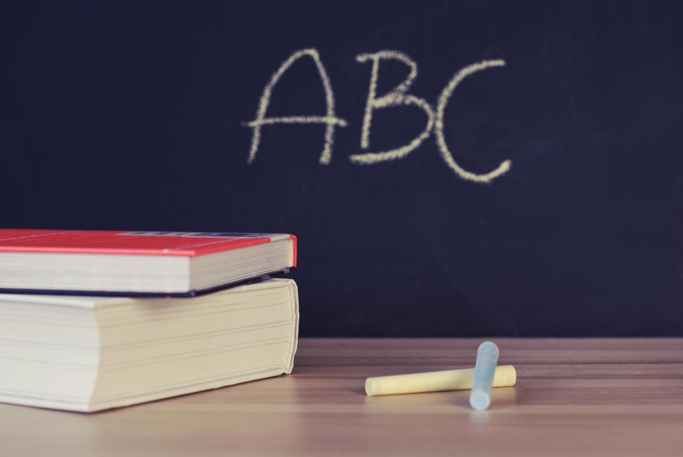 Free Image of Stack of books with chalks and ABC drawn on a blackboard background. 