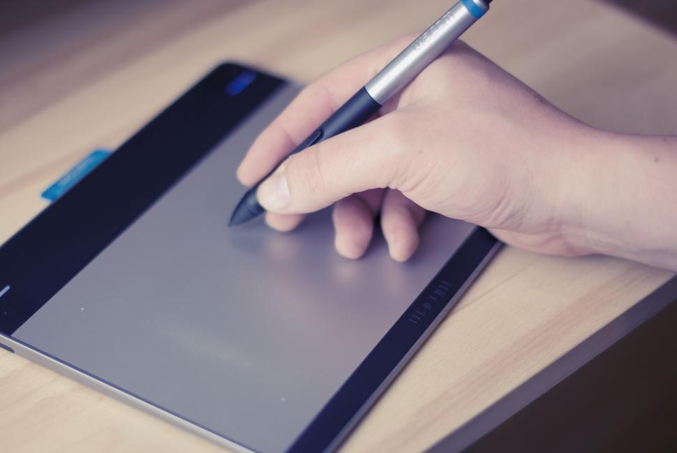 Free Image of Hand holding stylus pen over a digital drawing tablet on a desk. 