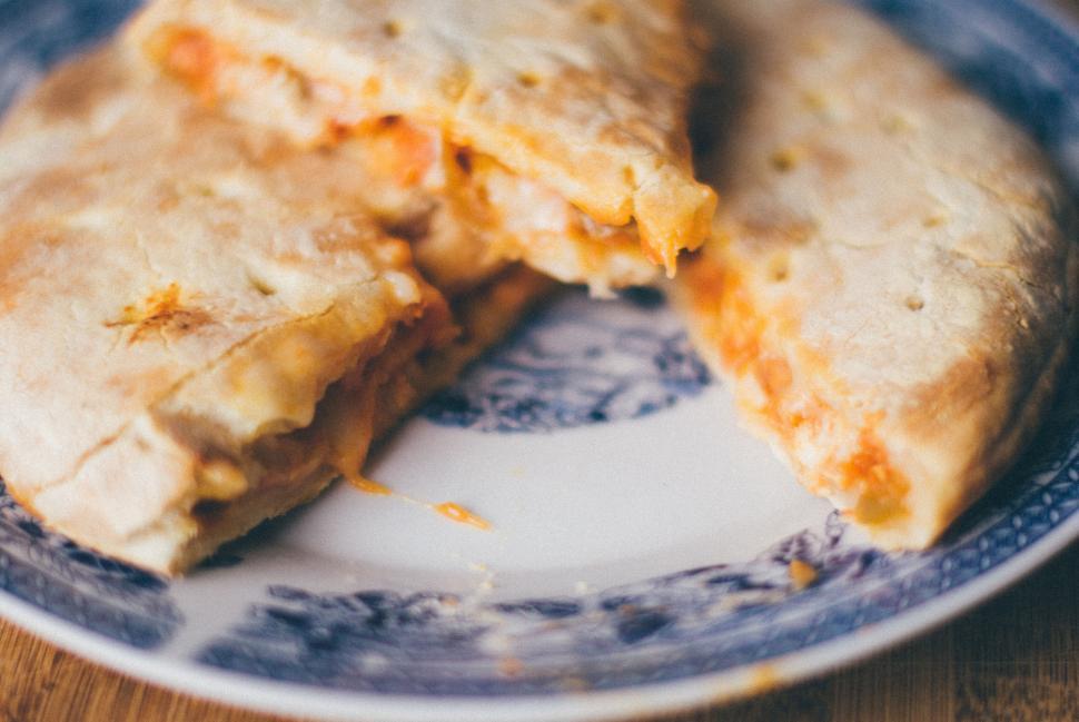 Free Image of Sliced cheesy calzone with visible fillings on a decorative blue plate. 