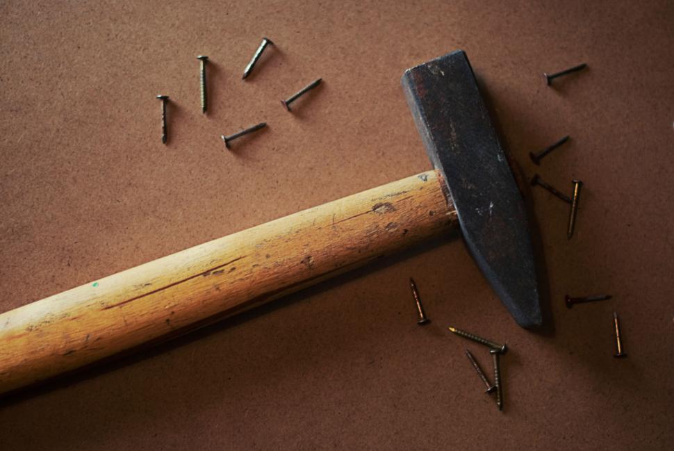 Free Image of Hammer with nails scattered on a brown wooden surface. 