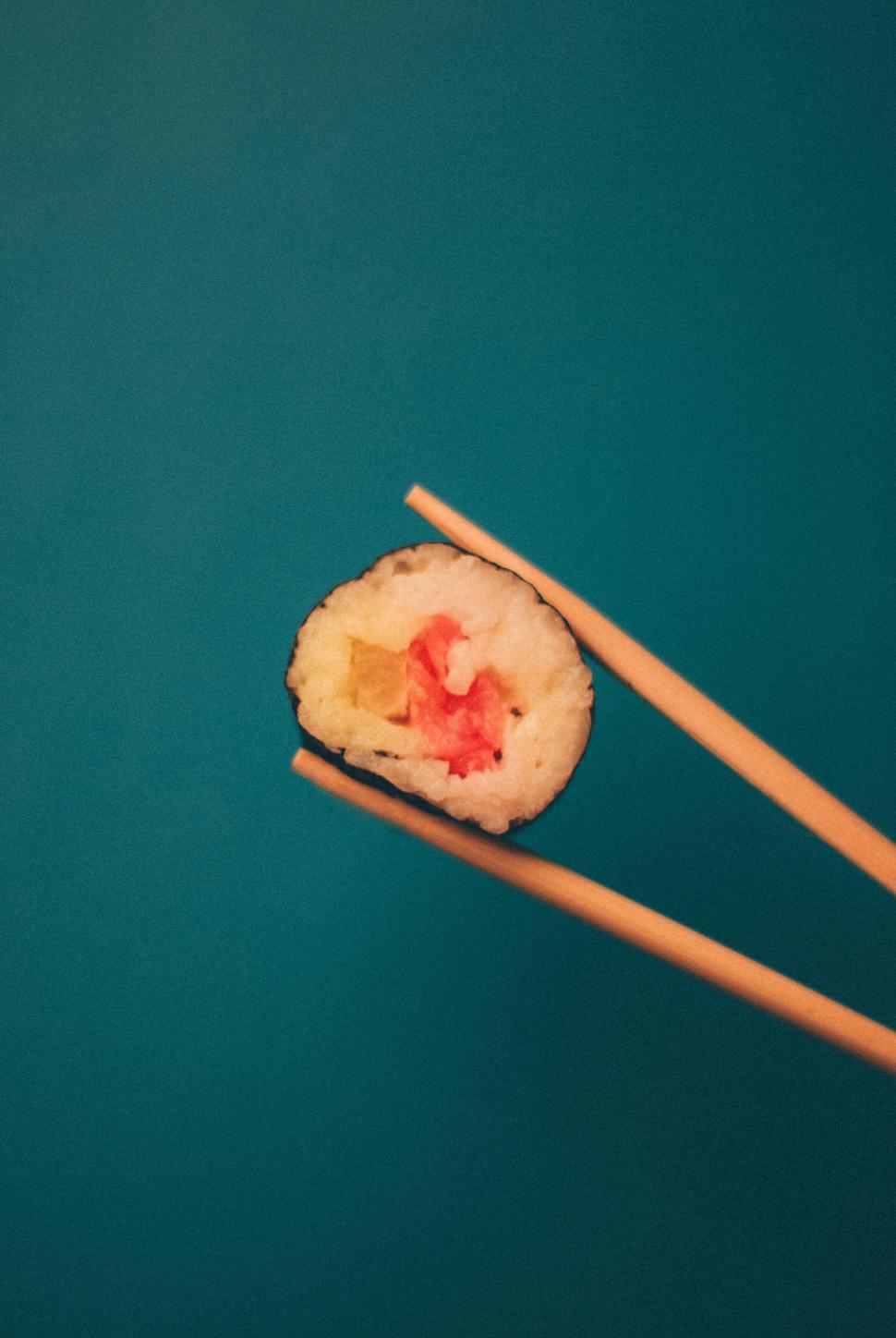 Free Image of Fresh sushi held by chopsticks against a blue background. 