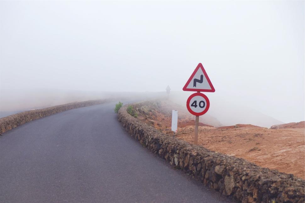 Free Image of Winding road with speed limit sign on a foggy day in mountains 