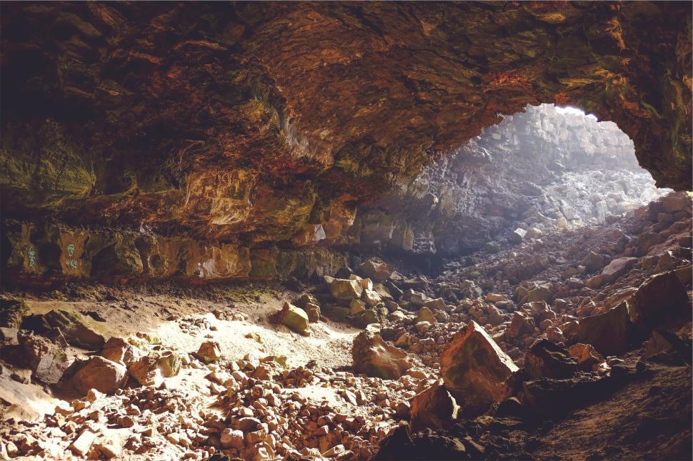 Free Image of Sunlit cave entrance revealing rocky ground and stone formations 