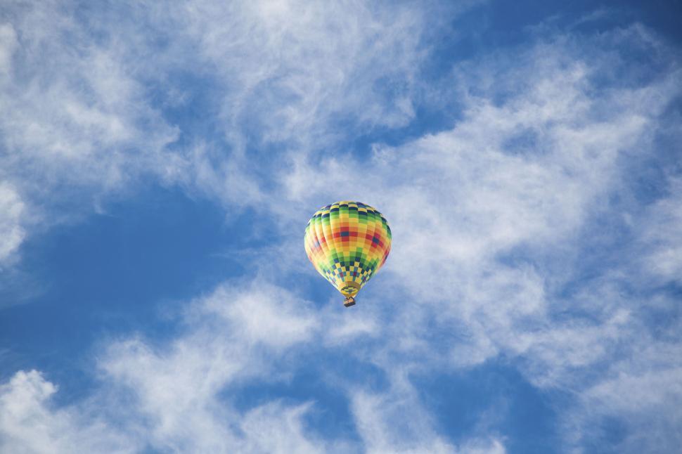 Free Image of Brightly colored hot air balloon soaring through a cloudy sky 