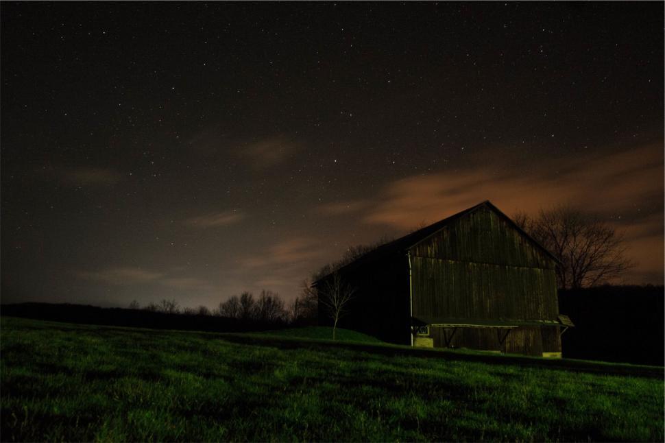 Free Image of Wooden barn under starry night sky and subtle orange-tinted clouds 