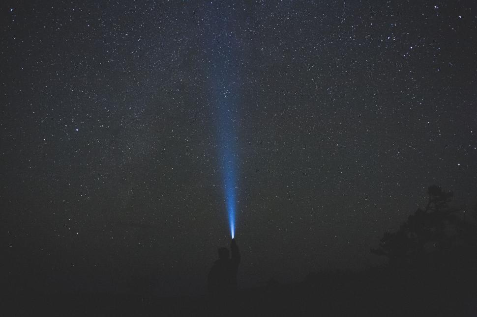 Free Image of Person shining flashlight beam into star-filled night sky outdoors 