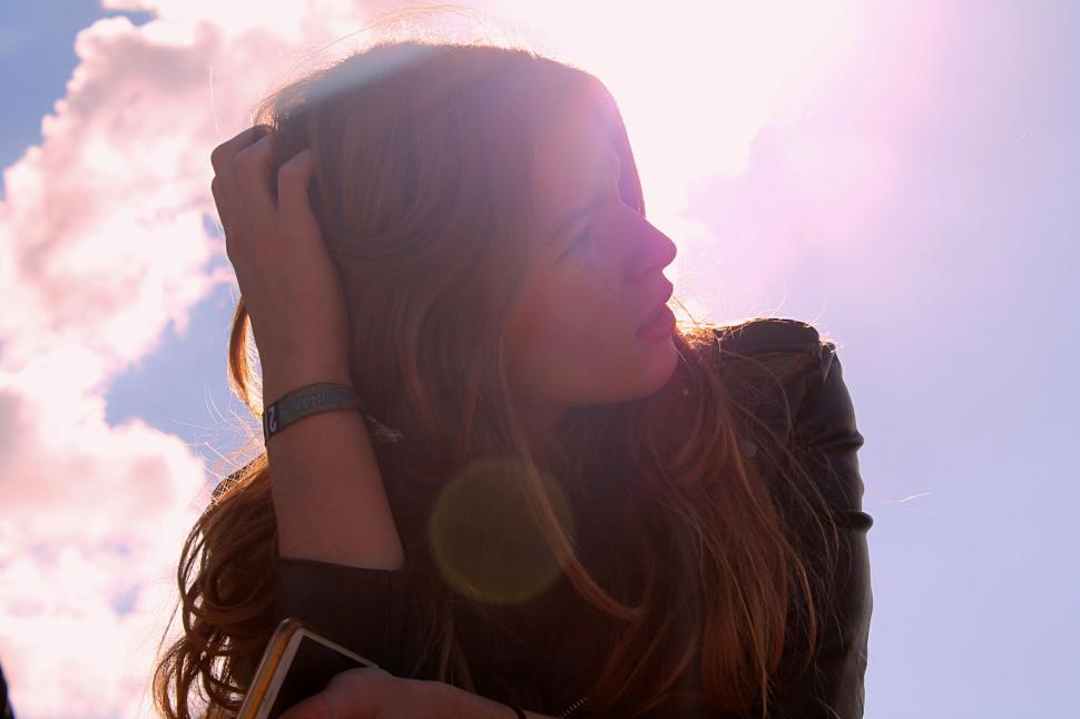 Free Image of Person standing outdoors under sunlight, holding their head in hand 