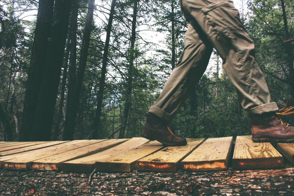 Free Image of Person walking on wooden path through forest, legs in focus only. 