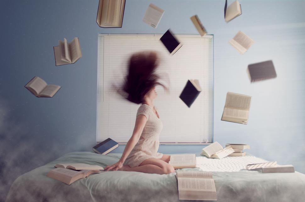 Free Image of Woman on bed with floating books around, dramatic hair movement. 
