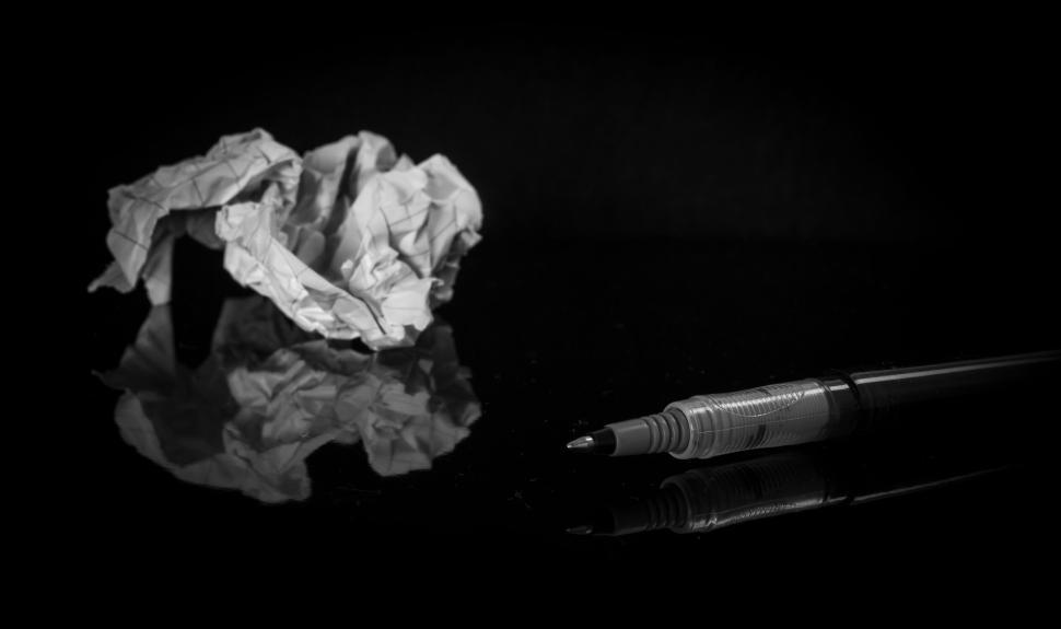 Free Image of Crumpled paper and pen on reflective black surface in darkness 