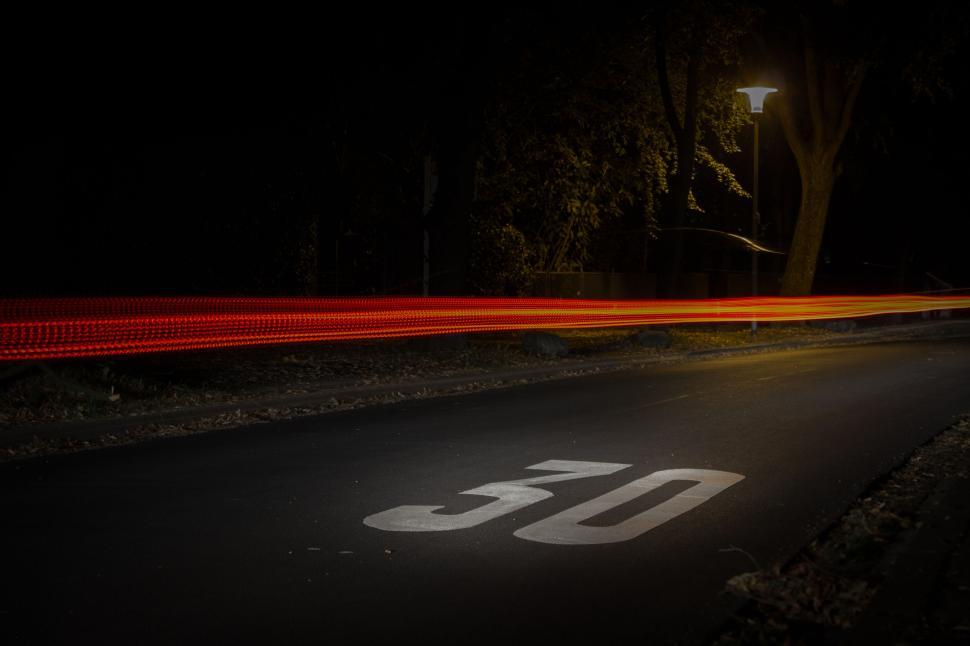 Free Image of Street with 30 speed limit mark and light streak from passing car 
