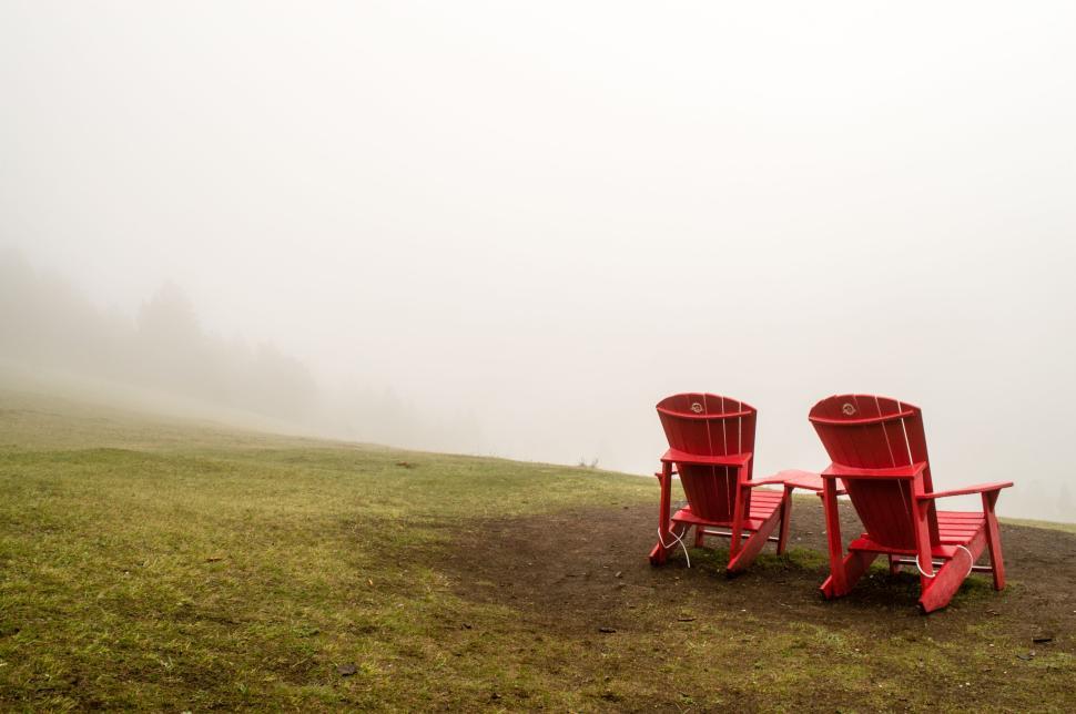 Free Image of Two red Adirondack chairs facing nature in a foggy setting 