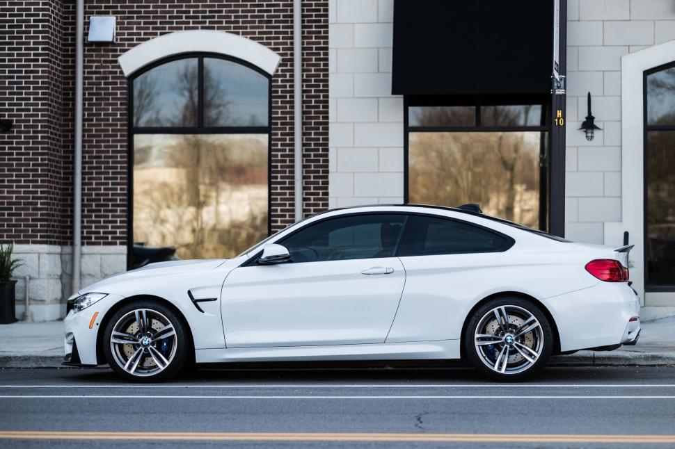Free Image of White luxury coupe parked on street near brick and stone building 