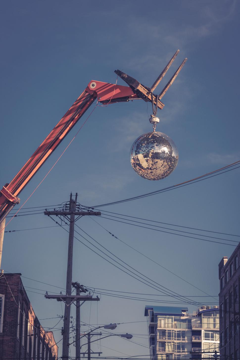 Free Image of Crane holding a disco ball high above urban street against blue sky. 