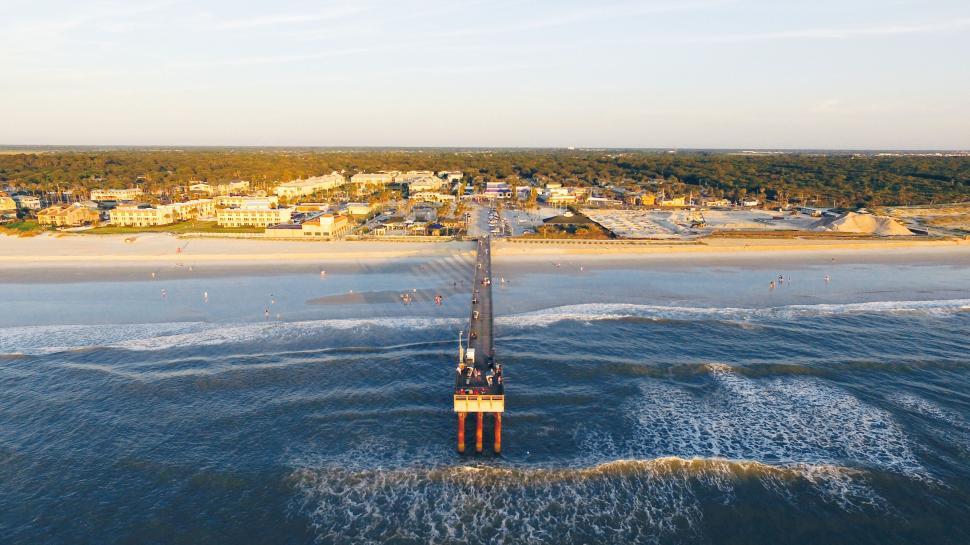 Free Image of Aerial view of pier extending into ocean with a coastal cityscape 