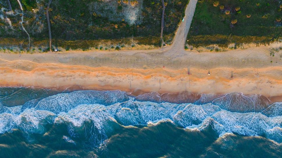 Free Image of Aerial view of waves crashing onto a sandy and scenic shoreline 