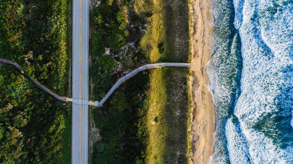 Free Image of Aerial shot of boardwalk and road beside beach with crashing waves. 
