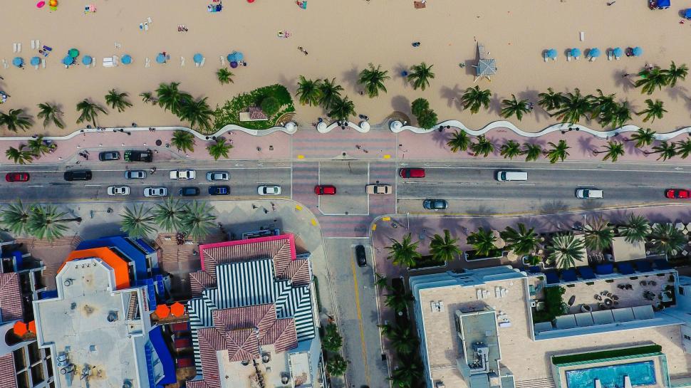 Free Image of Aerial view of a vibrant beach with a road alongside and cars moving by 