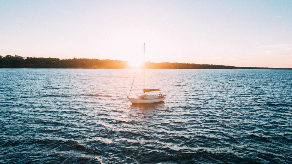 Free Image of A lone sailboat drifts on serene waters with a sunset in view. 