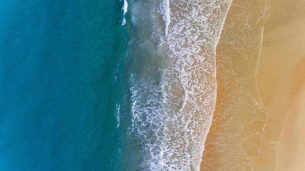 Free Image of Aerial shot of a shoreline detailing waves meeting the sandy beach. 