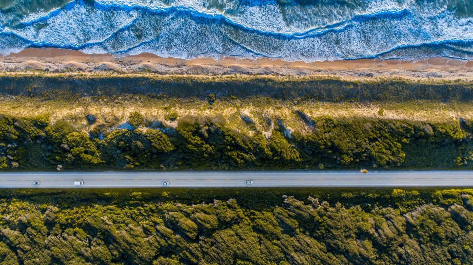 Free Image of Coastal road beside ocean waves crashing onto the sandy beach 