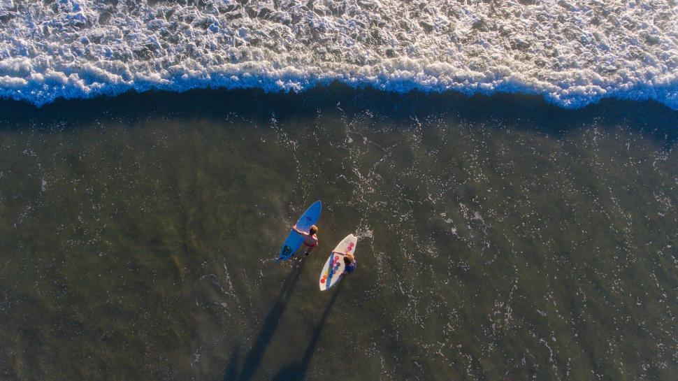 Free Image of Surfers paddling in water towards ocean waves on a sunny day 